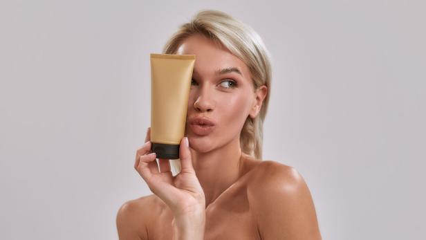 Eine Frau hält eine goldene Tube vor ihr Gesicht und schaut zur Seite.