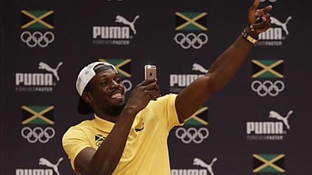 Usain Bolt macht ein Selfie vor einem Hintergrund mit jamaikanischen Flaggen und Puma-Logos.