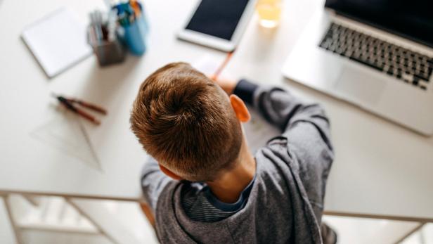 Ein Kind macht Hausaufgaben an einem Schreibtisch mit Laptop und Tablet.