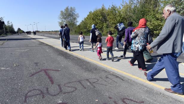Eine Gruppe von Menschen, darunter Kinder, geht auf einer Straße mit der Aufschrift „Austria“.