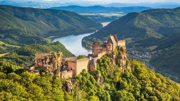 Die Burgruine Aggstein thront über der Donau, umgeben von bewaldeten Hügeln.