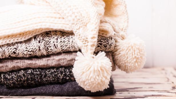 Ein Stapel gestrickter Schals und eine Mütze mit Bommeln.