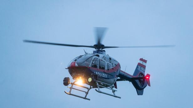 Ein rot-blau-weisser Polizei-Hubschrauber mit der Kennung OE-BXA ist in der Luft.