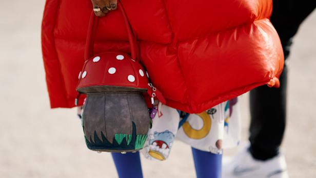 Eine Person mit einer roten Pufferjacke hält eine Handtasche in Form eines Fliegenpilzes.