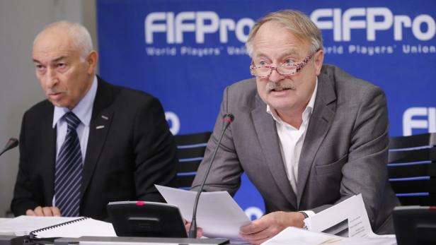 Zwei Männer sitzen an einem Tisch vor einem FIFPro-Banner.