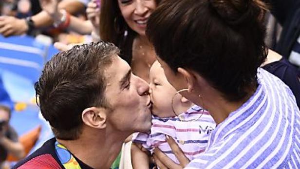 Michael Phelps küsst sein Kind, das von seiner Frau gehalten wird.