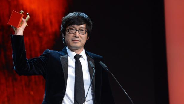 Ein Mann mit Brille im Anzug hält eine Auszeichnung in die Höhe.