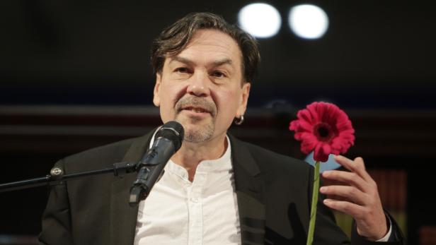 Ein Mann mit Mikrofon hält eine rote Gerbera in der Hand.