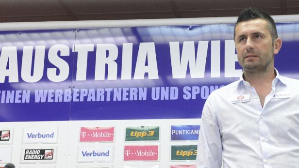 Ein Mann steht vor einer Wand mit dem Logo des FK Austria Wien und Sponsorenlogos.