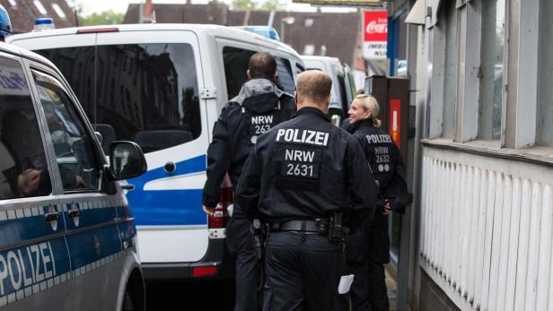 Mehrere Polizisten der NRW-Polizei stehen vor einem Gebäude.