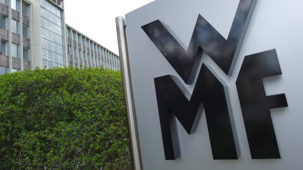 Das Logo von WMF vor einem Bürogebäude und einer grünen Hecke.