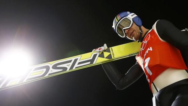 Ein Skispringer mit Helm und Skibrille hält seine gelben Fischer-Ski.