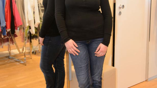 Eine Frau in Jeans und einem schwarzen Oberteil posiert vor einem Spiegel in einem Geschäft.