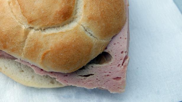 Ein Brötchen mit einer Scheibe Fleischwurst auf einem weißen Papieruntergrund.