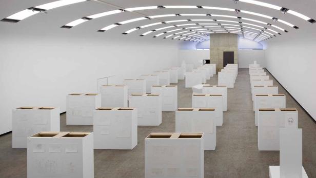 Ein Ausstellungsraum mit weißen Sockeln, auf denen Zeichnungen präsentiert werden.