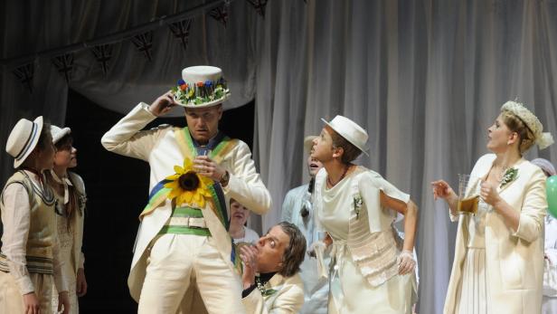 Eine Theaterszene mit mehreren Darstellern in weißen Kostümen und Hüten.