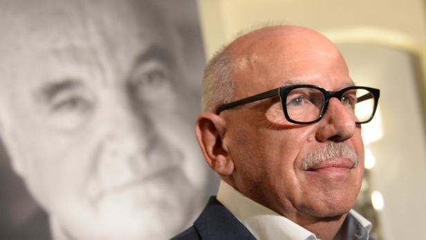 Ein Mann mit Brille und Schnurrbart vor einem unscharfen Porträt.