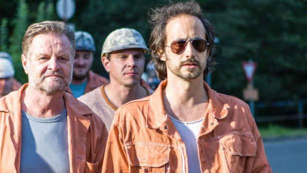Mehrere Männer in orangefarbenen Overalls stehen im Freien.
