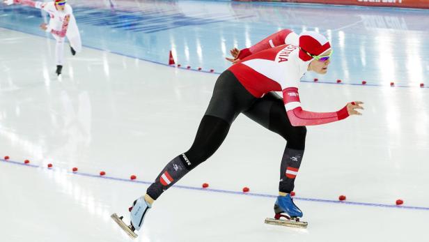 Eine Eisschnellläuferin im rot-weißen Anzug während eines Rennens.