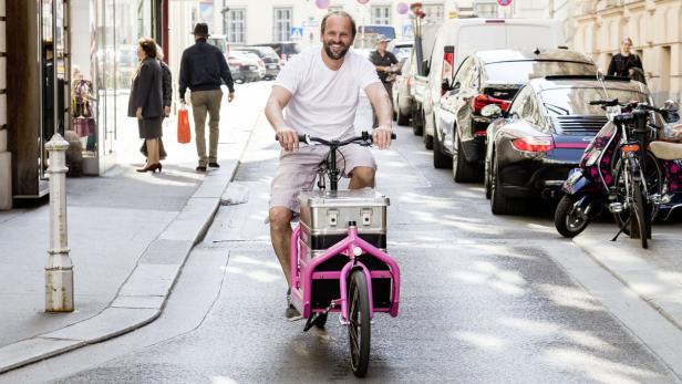 Ein Mann fährt mit einem pinkfarbenen Lastenfahrrad auf einer Straße.