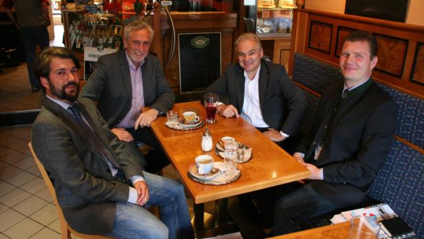 Vier Männer sitzen an einem Tisch in einem Café und trinken Kaffee.