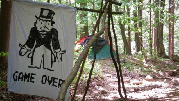 Im Wald hängt ein Banner mit der Aufschrift „Game Over“ und einer Zeichnung der Monopoly-Figur.