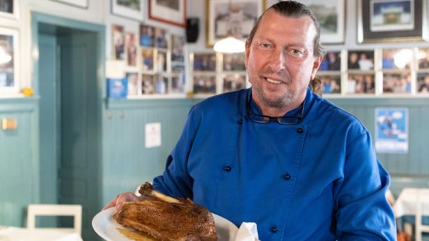 Ein Koch in blauer Uniform präsentiert eine gebratene Gans auf einem Teller.