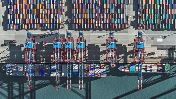 Luftaufnahme von Containerschiffen und Kränen in einem Hafen.