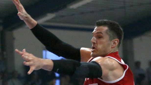 Ein Basketballspieler mit roten Trikot und Armstulpen streckt die Arme aus.