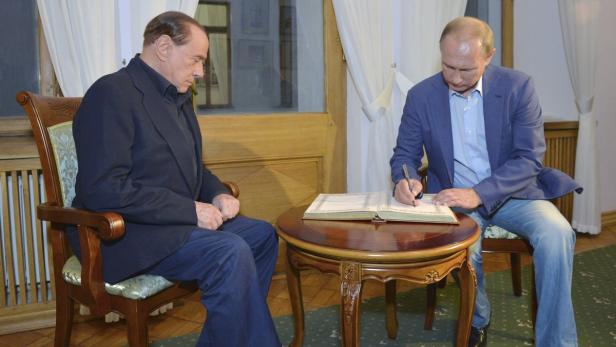 Wladimir Putin unterschreibt in Anwesenheit von Silvio Berlusconi ein Dokument.