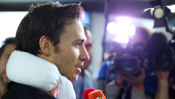 Ein Mann mit Nackenkissen wird von Reportern interviewt.