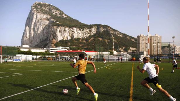 Fußballspieler trainieren auf einem Platz mit dem Felsen von Gibraltar im Hintergrund.