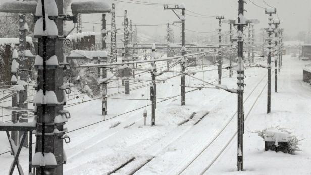 Eine verschneite Bahntrasse mit Oberleitungen und Masten im Winter.