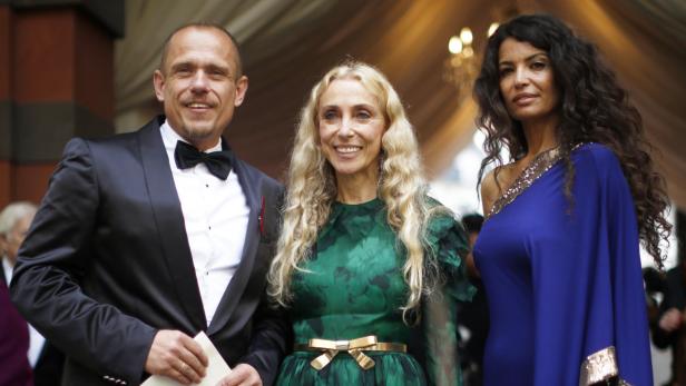 Drei Personen posieren für ein Foto, eine im Smoking, eine in einem grünen Kleid und eine in einem blauen Kleid.