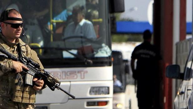 Ein bewaffneter Soldat steht vor einem Bus und einem Polizeiwagen.