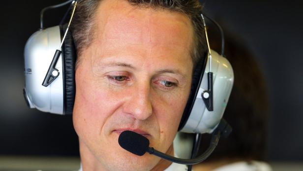 Michael Schumacher mit Kopfhörern und Mikrofon, den Blick nach unten gerichtet.