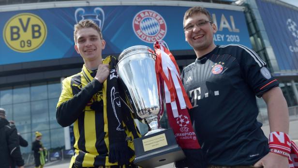 Zwei Fußballfans mit Schals von Borussia Dortmund und Bayern München halten die Champions-League-Trophäe 2013.
