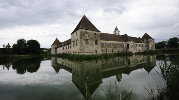 Ein Schloss mit Wassergraben spiegelt sich im ruhigen Wasser.
