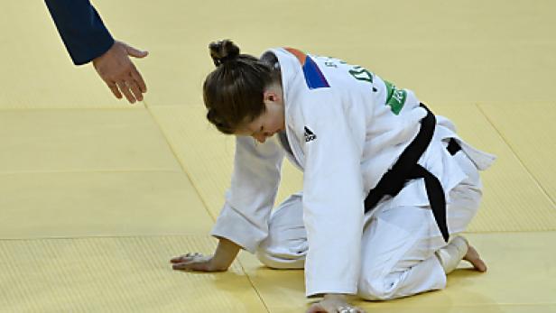Eine Judoka kniet enttäuscht auf der Matte, während ein Schiedsrichter ihr die Hand reicht.