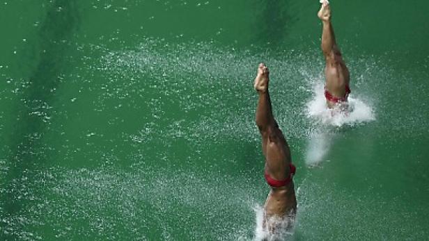 Zwei Synchronschwimmerinnen springen gleichzeitig ins grüne Wasser.