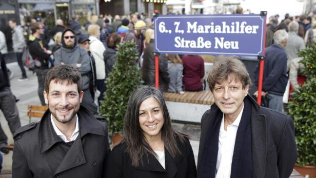 Drei Personen posieren vor einem Schild „6., 7., Mariahilfer Straße Neu“.