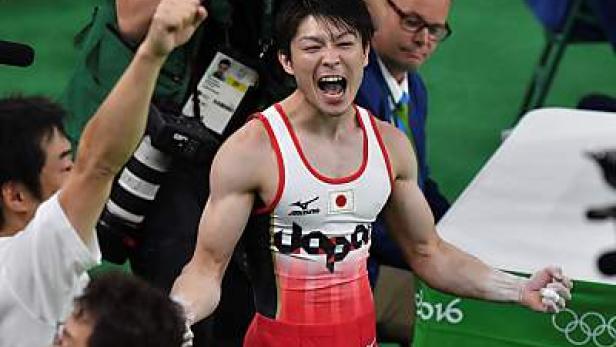 Ein japanischer Turner jubelt mit geballten Fäusten und geöffnetem Mund bei einem Wettkampf.