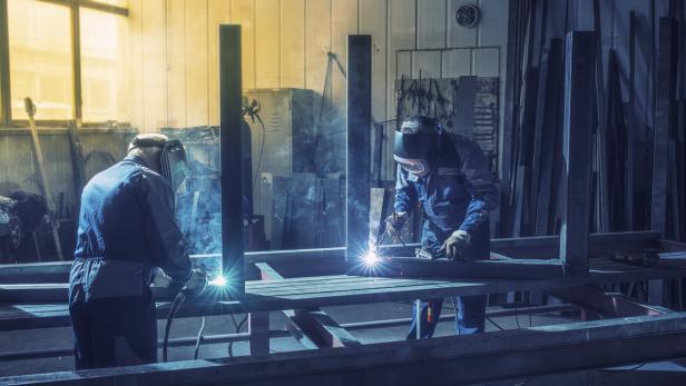 Zwei Schweißer arbeiten in einer Werkstatt an einer Metallkonstruktion.