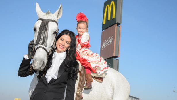 Eine Frau und ein Mädchen auf einem Schimmelpferd vor einem McDonald's-Schild.