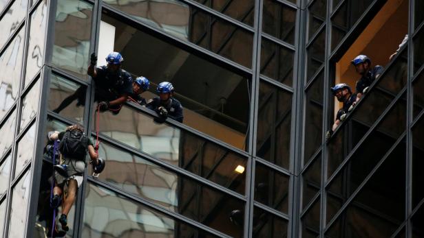 Ein Mann seilt sich an einem Hochhaus ab, während Polizisten aus den Fenstern schauen.