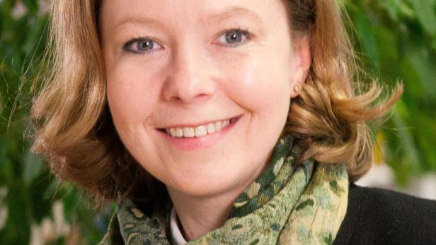 Eine lächelnde Frau mit blonden Haaren und einem grünen Schal vor einem grünen Hintergrund.