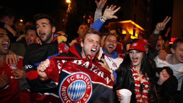 Eine Gruppe jubelnder Fußballfans des FC Bayern München feiert auf der Straße.