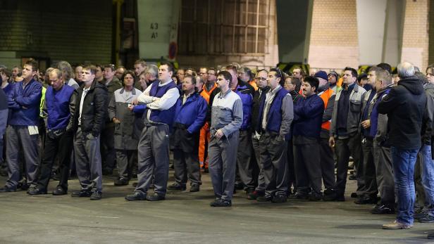 Eine Gruppe von Arbeitern steht in einer Fabrikhalle und schaut in die Ferne.
