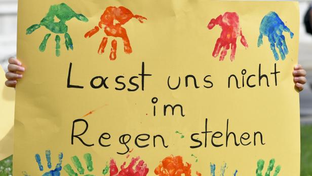 Ein gelbes Schild mit bunten Handabdrücken und der Aufschrift „Lasst uns nicht im Regen stehen“.