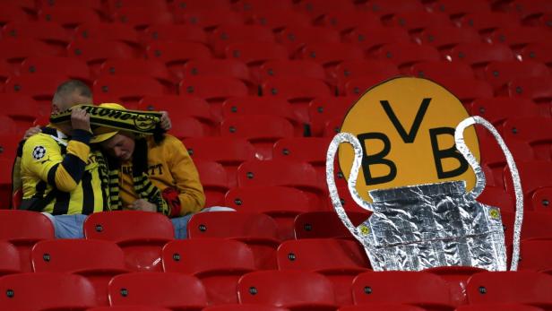 Zwei enttäuschte Borussia Dortmund Fans sitzen im Stadion neben einem Papppokal.